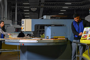 Workers operate machinery in a manufacturing facility, showcasing teamwork and production processes.