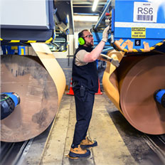 Worker operating machinery in a manufacturing facility, focusing on large rolls of material and safety precautions.