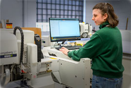 A technician operates a computer connected to a machine in a modern workshop setting.