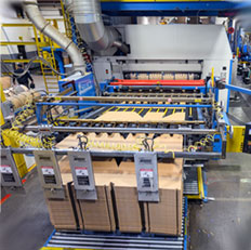 Automated machinery in a factory efficiently processes and stacks cardboard boxes for packaging.