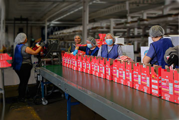 Workers in a factory assembling red boxes on a conveyor belt, showcasing teamwork and production efficiency.