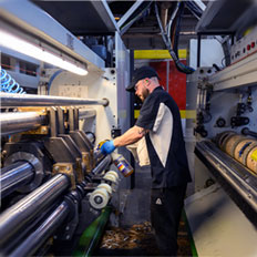 A worker operates machinery in a manufacturing facility, focusing on maintenance and cleaning tasks.
