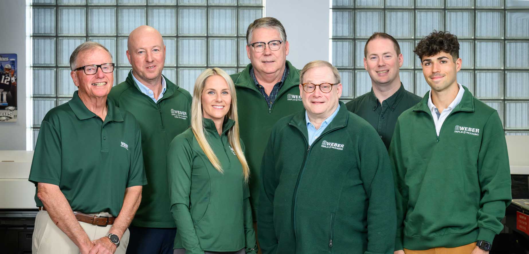 Seven team members in green jackets pose together, showcasing their unity and professionalism for the "Who We Are" page.