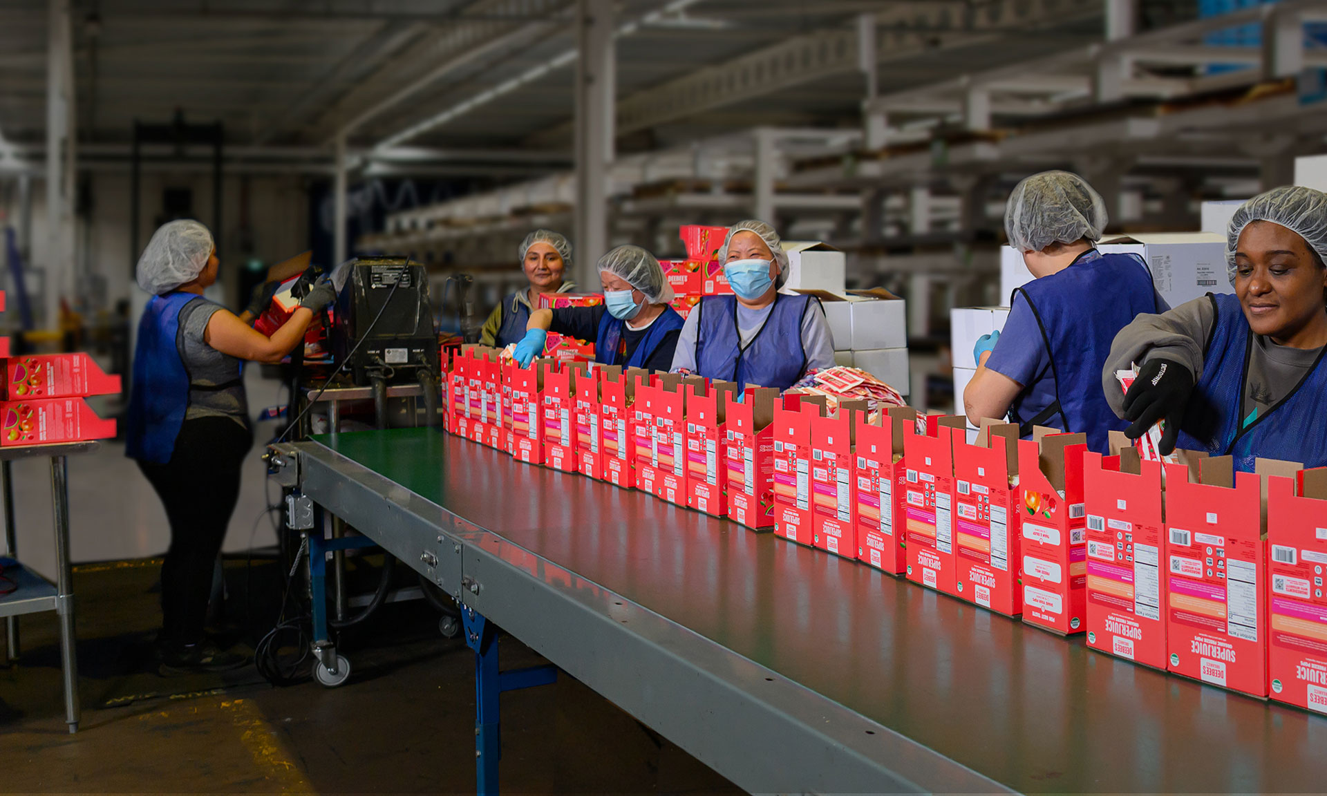 Workers in a warehouse assemble and package red boxes on a conveyor belt for industrial packaging.