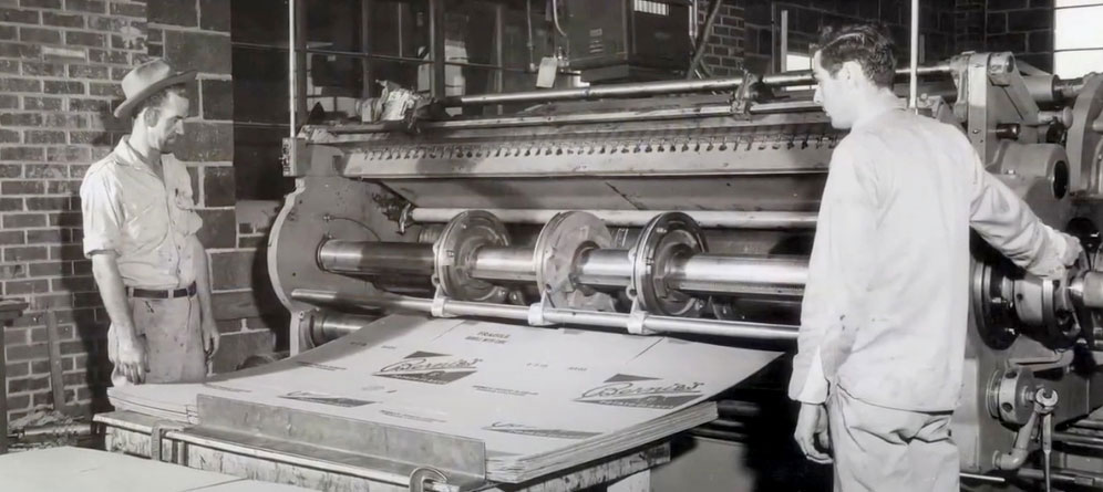 Two workers operate a vintage printing press, showcasing historical printing techniques and machinery.